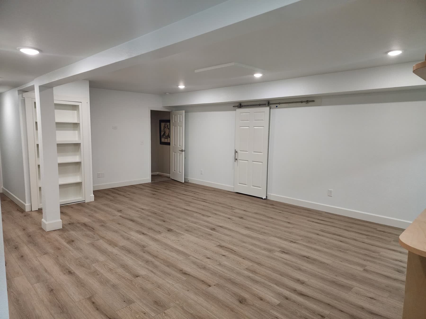 Finished basement with LVP flooring, built-in shelving and a sliding barn door