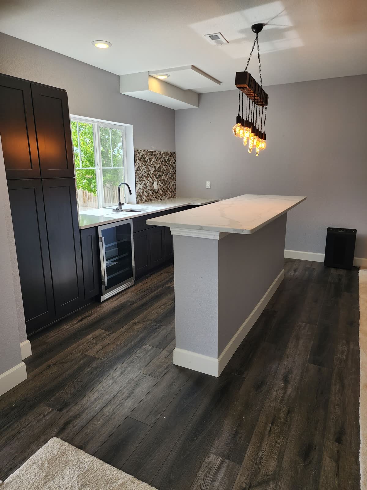 Wet bar with dark cabinets and pendant light